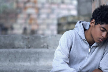 Depressed male teenager leaning brick wall sitting stairs, domestic violence