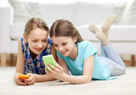 2 happy girls playing smartphones while lying on the floor